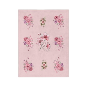 Peut inclure: Une couverture en polaire rose pâle ornée d'un motif répétitif de bouquets de fleurs. Le design comprend six grappes de roses roses et violettes disposées autour d'une illustration centrale plus grande de fleurs de cerisier rose clair.