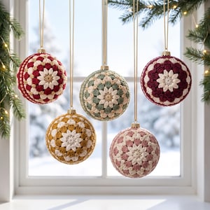 Op de afbeelding: Vijf bolvormige kerstballen met ingewikkelde gehaakte hoezen met bloemachtige patronen. De kerstballen hangen aan gouden koordjes en vertonen diverse kleurcombinaties, waaronder rood, crème, saliegroen, mosterdgeel en oudroze.