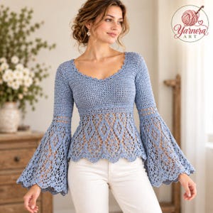 May include: A light blue long-sleeve crochet top featuring a scalloped neckline and intricate diamond-patterned lace detailing on the bodice and flared bell sleeves. The garment is paired with white pants and includes a Yarnora Art logo.