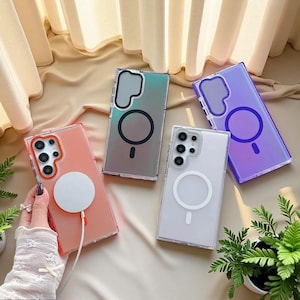 May include: Four rectangular smartphone cases with magnetic charging rings on the back. One case is coral with a white magnetic charger attached, one is iridescent silver, one is clear, and one is purple. Each case features a camera cutout.