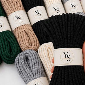 May include: A collection of multi-coloured macrame cord bundles arranged in rows. Each bundle is secured with a white paper band featuring the black text YS. The colours include dark green, beige, black, cream, grey, pink, brown, yellow, and purple.