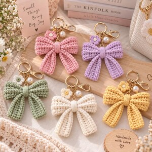 Può includere: Cinque portachiavi a forma di fiocco all'uncinetto nei colori rosa, lavanda, verde salvia, crema e giallo. Ogni portachiavi presenta un anello in metallo dorato, un moschettone, una piccola perla bianca e un minuscolo fiore all'uncinetto.