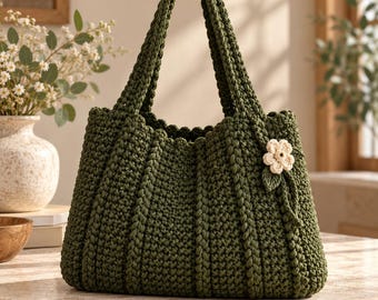 May include: A dark olive green crochet tote bag featuring a textured ribbed pattern and two sturdy handles. A small, cream-colored crocheted flower with a single green leaf is attached to the front right side of the bag as a decorative accent.