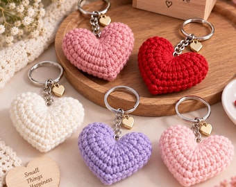 May include: Five crochet heart keychains in pink, red, white, purple, and light pink. Each keychain features a silver metal ring, a small gold heart charm, and a textured yarn heart. A wooden block displays the text Handmade with Love.