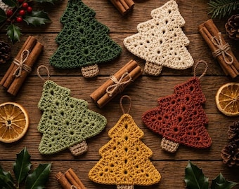May include: Five crocheted Christmas tree ornaments in dark green, cream, light green, mustard yellow, and rust red. Each tree features a small brown trunk and a hanging loop, arranged among cinnamon sticks, dried orange slices, and holly.