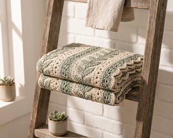 May include: A folded crochet blanket featuring alternating vertical stripes of sage green and cream yarn. The design includes a textured leaf pattern in the green sections and a delicate openwork stitch in the cream sections, finished with a scalloped edge.