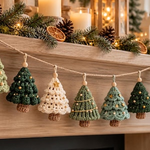 May include: A festive garland featuring seven crocheted Christmas tree ornaments in shades of sage green, dark forest green, and cream. Each tree is suspended from a natural jute twine string with a small wooden bead and brown trunk.