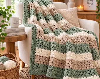 May include: A crocheted throw blanket featuring horizontal stripes in sage green, cream, and beige. The blanket has a textured, open-stitch pattern and is draped over a light-colored armchair. The design consists of repeating color blocks.