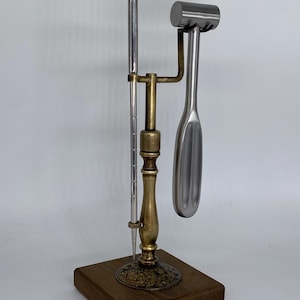 May include: A metal tool set with a wooden base. The set includes a long, slender tool with the word "FREEMAN" on the top, a hammer-like tool, and a spoon-shaped tool. The tools are made of silver and gold-colored metal.