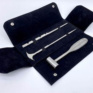 May include: A set of three surgical tools in a black leather case. The tools include a hammer, a hook, and a long, thin tool with a pointed end.
