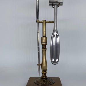 May include: A vintage bar tool set with a wooden base. The set includes a metal ice pick, a muddler, and a bottle opener. The bottle opener has the word "FREEMAN" engraved on it. The tools are made of silver and brass.