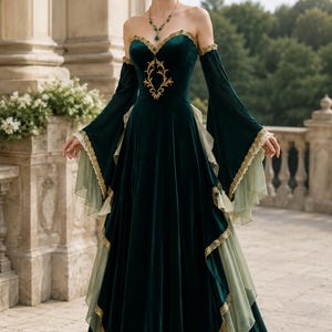 Puede incluir: Un vestido largo de terciopelo verde oscuro con escote descubierto, mangas largas acampanadas con volantes verde claro y bordados dorados en el corpiño. El vestido incluye paneles de tela verde claro superpuestos y ribetes dorados.