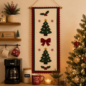 May include: A rectangular crochet wall hanging featuring a cream-colored background with a dark green border and a scalloped red edge. The design includes two green Christmas trees, a red bow, holly berries, and small red snowflake accents.