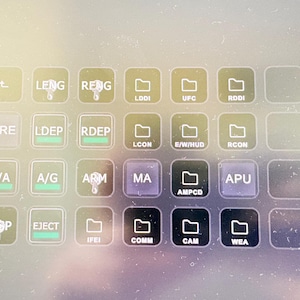 May include: A digital interface screen displaying a grid of square buttons with white text labels including LENG, RENG, FIRE, LDEP, RDEP, A/A, A/G, ARM, MA, APU, DISP, EJECT, and various folder icons labeled LDDI, UFC, RDDI, LCON, E/W/HUD, RCON, AMPCD, IFEI, COMM, CAM, and WEA.