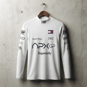 May include: A white long-sleeve mock neck shirt featuring various black sponsor logos and text including OMP, Tommy Hilfiger, Swart Ninja, IWC, APX GP, and Expensify. The shirt is displayed on a wooden hanger against a textured gray concrete wall.