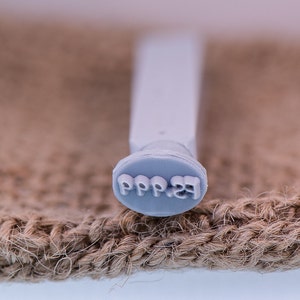 May include: A close-up of a gray rubber stamp with the text "PPP.23" on it. The stamp is sitting on a brown burlap surface.