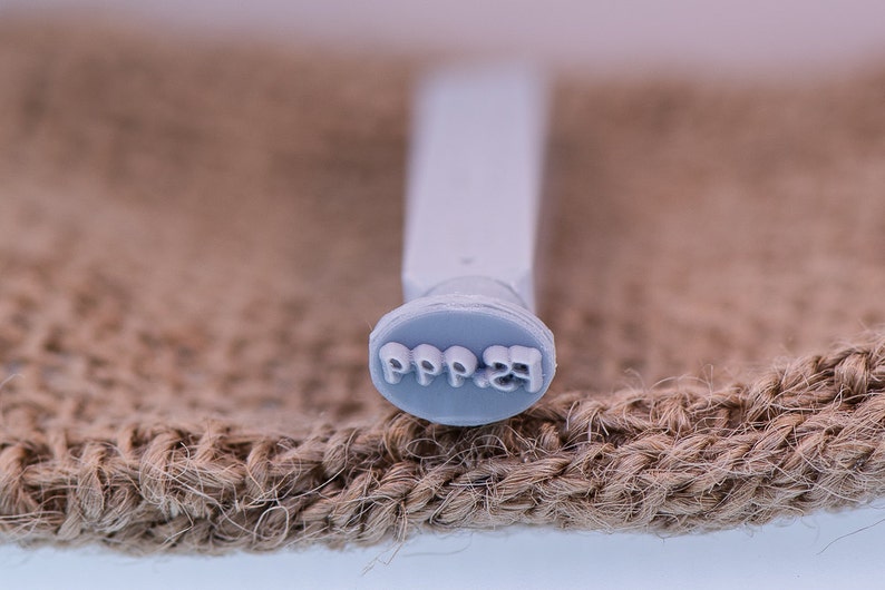 May include: A close-up of a gray rubber stamp with the text "PPP.23" on it. The stamp is sitting on a brown burlap surface.
