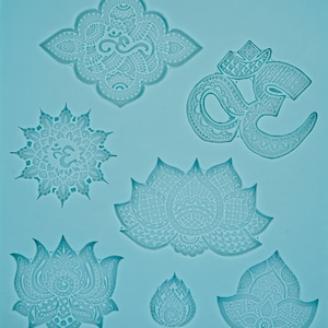 Pode incluir: Um molde de silicone azul com seis designs diferentes: um mandala com o símbolo Om, uma flor de lótus, um símbolo Om estilizado e três designs diferentes de flores de lótus. O molde é para fazer joias ou outras manualidades.