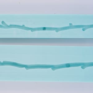 Puede incluir: Dos moldes de silicona azul claro para hacer decoraciones de pasteles. Cada molde presenta un diseño en relieve de una rama con una forma natural e irregular.
