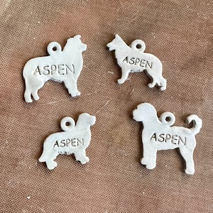 Może przedstawiać: Cztery białe ceramiczne ozdoby w kształcie psa, każda z napisem "Aspen".