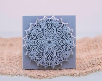 May include: A gray square tile with a raised, intricate, white mandala design.