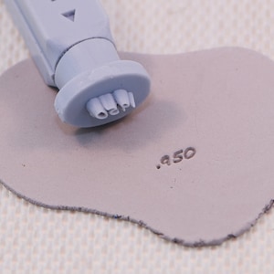 May include: A close-up of a grey clay stamp with the text "02PI" and a number "950" stamped into the clay.