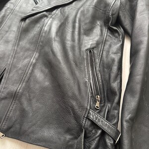 May include: Black leather jacket with an asymmetrical zipper closure, a notched lapel, and a zippered chest pocket. The jacket has a belt detail at the waist and a classic biker style.