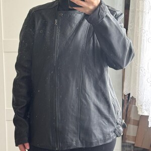 May include: Black leather jacket with an asymmetrical zipper closure and a high collar. The jacket has a fitted silhouette, long sleeves, and a buckle detail at the waist. The jacket appears to be made of a smooth, possibly genuine leather material.