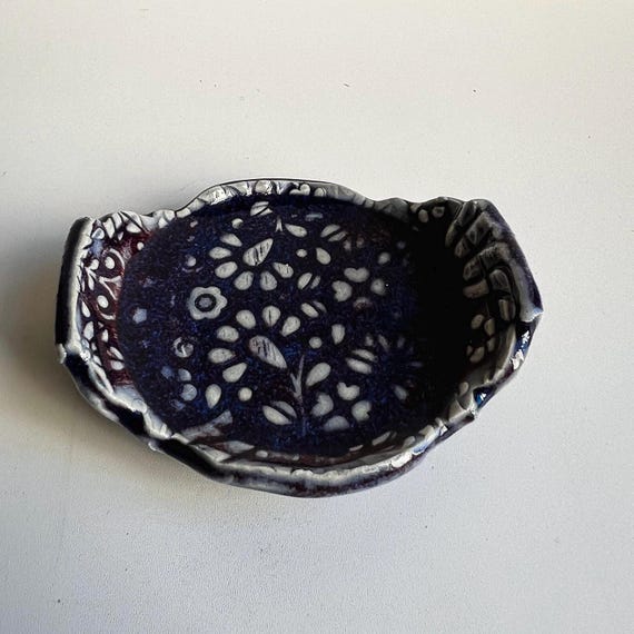 Footed cobalt-blue studio pottery dish with botanical detailing — the kind of small object that becomes the most-noticed thing on a vanity.