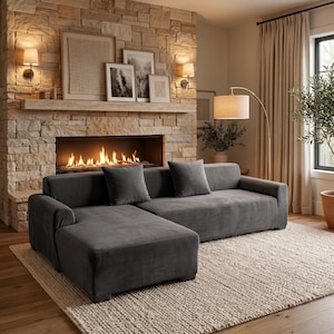 May include: A charcoal gray velvet sectional sofa featuring a chaise lounge on the left side and two matching square throw pillows. The sofa has a low-profile design with clean lines and a smooth, soft-textured fabric finish throughout the frame.