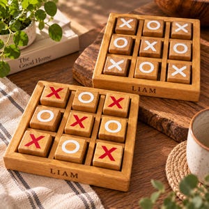 May include: Two square wooden tic-tac-toe game boards with a grid frame. Each board features the name LIAM engraved on the front edge. One board contains wooden blocks with white X and O symbols, while the other has blocks with red X and white O symbols.
