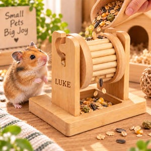 May include: A light-coloured wooden hamster feeder toy with a rotating drum mechanism. The side of the frame is engraved with the name LUKE. The feeder sits on a rectangular base and is filled with a mix of seeds, grains, and pellets.