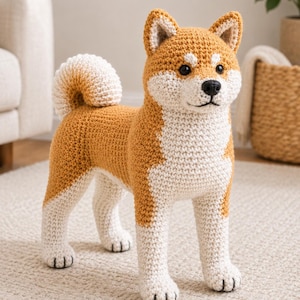 May include: A crochet stuffed animal shaped like a Shiba Inu dog. The toy features a golden-brown and white yarn pattern, a curled tail, black plastic eyes, and a black nose. The texture is consistent with hand-stitched yarn loops throughout the body.