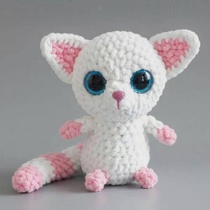 May include: A white and pink crocheted plush toy featuring large, glittery blue eyes, a small pink nose, and pointed ears. The creature has a long, striped tail, small paws, and a soft, textured yarn construction with a rounded head and body.
