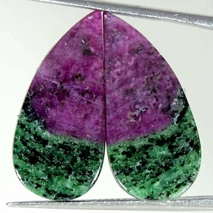 May include: A pair of pear-shaped ruby and zoisite gemstones featuring a distinct color split. The upper portion of each stone is a vibrant magenta-pink, while the lower section is a mottled forest green with dark black mineral inclusions.