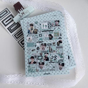 May include: A light blue sticker sheet featuring a collage of various small images, including portraits of individuals, chocolate-themed graphics, and text elements like "Chocolate," "mint," and "enhaçafe," accompanied by a matching binder clip.