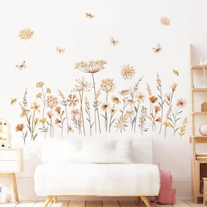 May include: A set of wall decals featuring watercolor-style illustrations of wildflowers, grasses, and various insects including butterflies and bees in soft shades of beige, brown, and muted pink, arranged in a meadow-like pattern on a white wall.