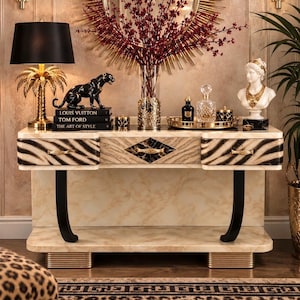 Peut inclure: Une console avec une finition en marbre crème, dotée de trois tiroirs aux façades rayées noir et blanc, d'une incrustation centrale en marbre noir en forme de losange et de deux pieds noirs incurvés avec des accents dorés à la base.