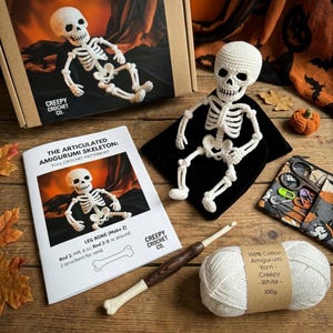 Pode incluir: Um kit de crochê contendo um esqueleto amigurumi branco, um livreto de padrões intitulado The Articulated Amigurumi Skeleton, uma agulha de crochê de madeira, um novelo de 100g de fio de algodão branco e um estojo com ferramentas de costura.