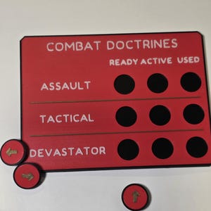 May include: A rectangular red game board with black circular slots and white text reading COMBAT DOCTRINES, READY, ACTIVE, USED, ASSAULT, TACTICAL, and DEVASTATOR. Three small red circular tokens with gold arrows are placed near the board.