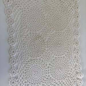 May include: A rectangular off-white crochet doily featuring a repeating pattern of four circular motifs. The piece is finished with a delicate scalloped edge border, showcasing intricate thread work and openwork details throughout the design.