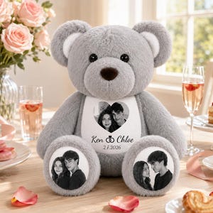 Könnte beinhalten: Ein grauer Plüschteddybär mit einem weißen Brustaufnäher, der ein herzförmiges Schwarz-Weiß-Foto eines Paares, den Text Ken and Chloe und das Datum 2.7.2026 zeigt. Der Bär hat runde weiße Aufnäher an den Füßen mit Schwarz-Weiß-Fotos.