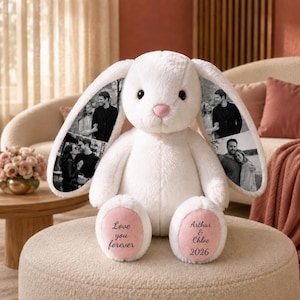 Può includere: Un coniglio di peluche bianco con lunghe orecchie decorate con fotografie in bianco e nero di coppie. Il coniglio ha un naso rosa e cuscinetti rosa sotto i piedi. Il piede sinistro riporta Love you forever e il destro Arthur & Chloe 2026.