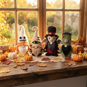 Op de afbeelding: Vier gehaakte kabouters in Halloween-thema: een witte geest met oranje accenten, een beige mummie met groene ogen, een vampier met een zwarte hoge hoed en cape, en een groen monster met één oog, allemaal voorzien van witte of zwarte baarden.