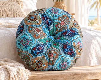 May include: A round, tufted throw pillow featuring a vibrant, multi-colored pattern with shades of turquoise, deep blue, brown, and red. The fabric displays intricate, symmetrical geometric and floral motifs, with a central fabric-covered button.