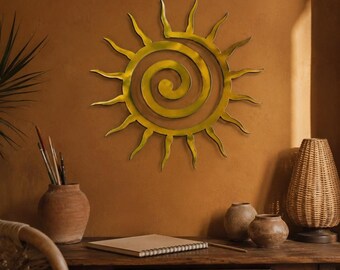 May include: A circular gold-toned metal wall art piece featuring a central spiral design surrounded by radiating wavy sun rays. The object is mounted on a solid, flat surface, showcasing a metallic finish with smooth, curved edges and a symmetrical form.