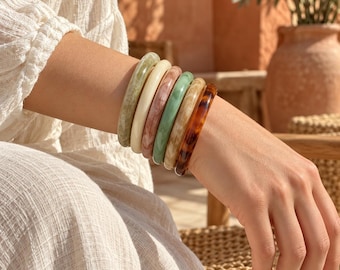 May include: A set of six stacked bangle bracelets featuring a variety of smooth, polished finishes including marbled sage green, solid cream, marbled mauve, solid mint green, marbled beige, and a dark brown tortoiseshell pattern.