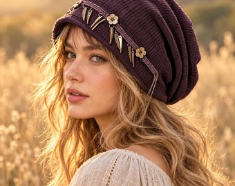 May include: A deep purple knit slouchy beanie featuring a decorative band adorned with metallic silver-toned flower charms and dangling leaf-shaped pendants. The hat has a ribbed texture and is worn over long wavy blonde hair.