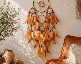 May include: A wall hanging dream catcher featuring a large central hoop with a tree of life design, surrounded by smaller hoops, turquoise-colored beads, and numerous long, light brown feathers hanging from the bottom in a layered arrangement.