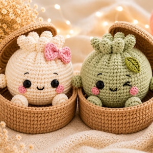 May include: Two round, crocheted plush toys shaped like dumplings, each nestled in a small, tan, circular woven basket. One is cream-colored with a pink bow, and the other is sage green with a small green leaf accent. Both have black eyes.